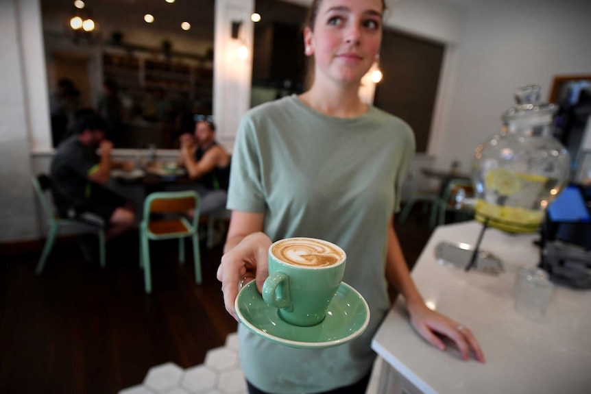 A waitrees looks to the side as she holds a cup of coffee balanced on a saucer
