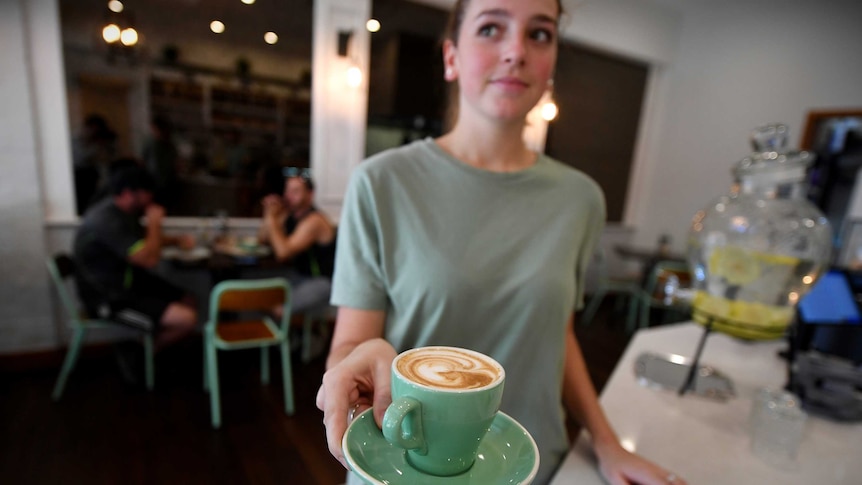 A waitress looks to the side as she holds a cup of coffee balanced on a saucer