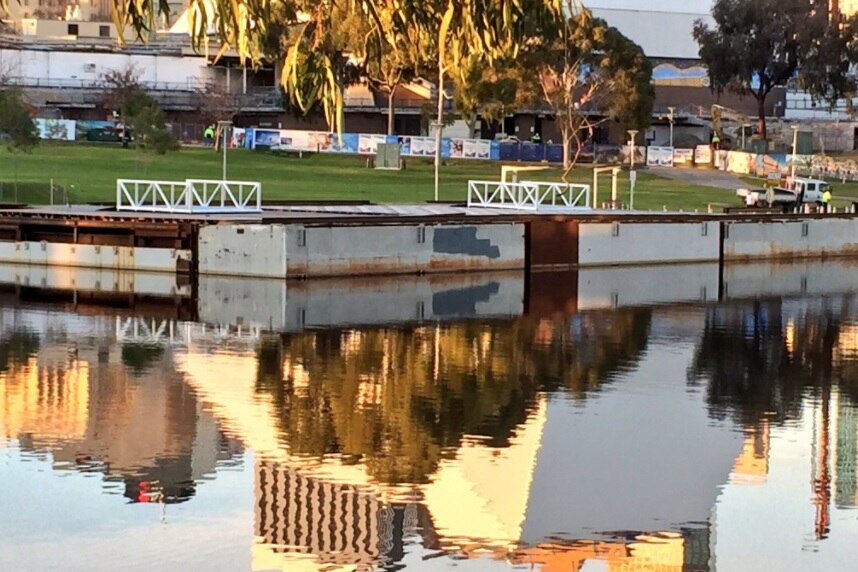 A pontoon floats in water with building reflections visible.