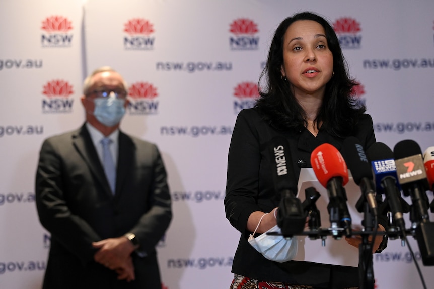 Dark-haired woman in dark suit speaks at microphone