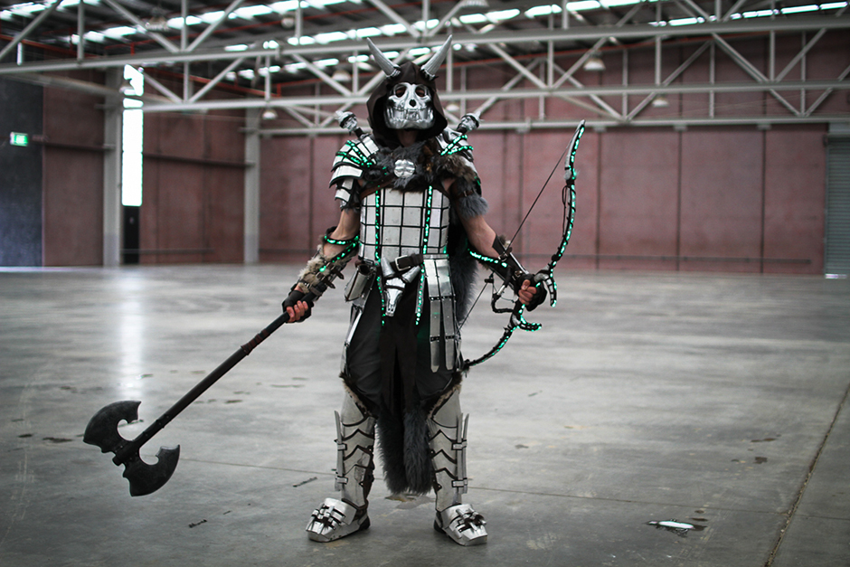 A man in green-highlighted armour and horned-skull mask, holding a large double-headed axe and a longbow.