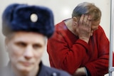 Sokolov in a red sweater has his hands buried in his face in despair, in front of him is a russian guard