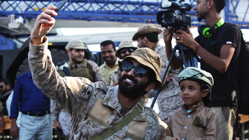 A Saudi soldier takes a photograph of himself with a young Yemeni boy in traditional dress