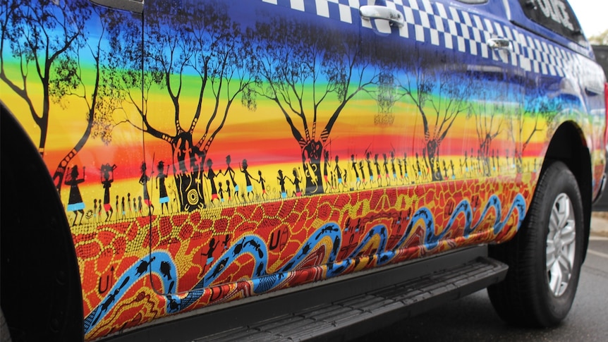 A police vehicle is covered in a rainbow Aboriginal art piece
