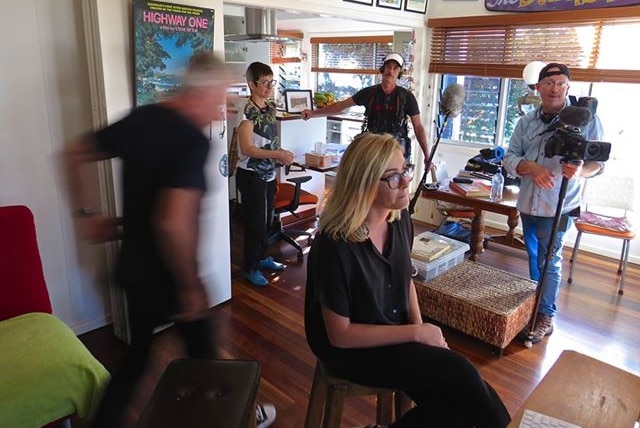 Journalist and film crew filming an interview for the television series in a loungeroom in a house.