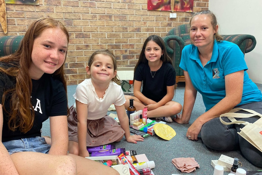 Three young girls and their mother with a pile of toiletries sitting on the floor in a living room.