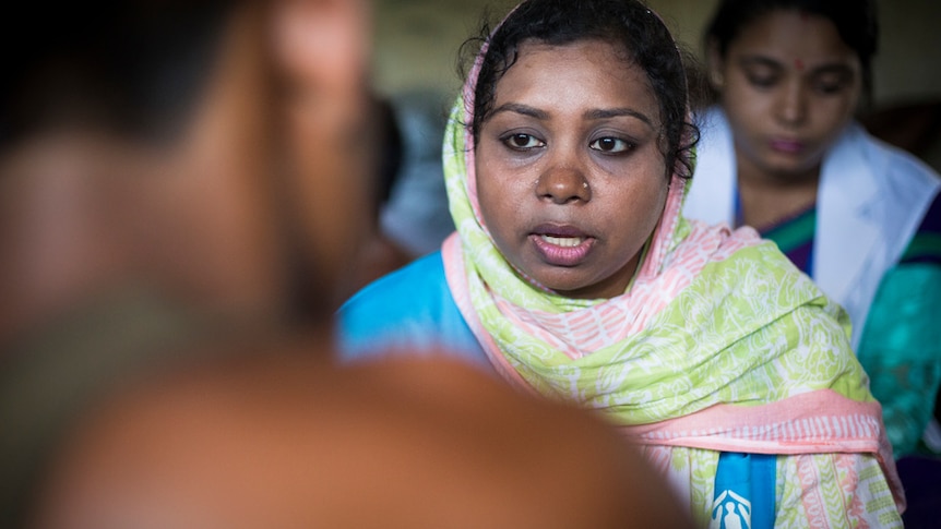 A UNHCR psychologist talks to a young refugee who has his back to the camera.