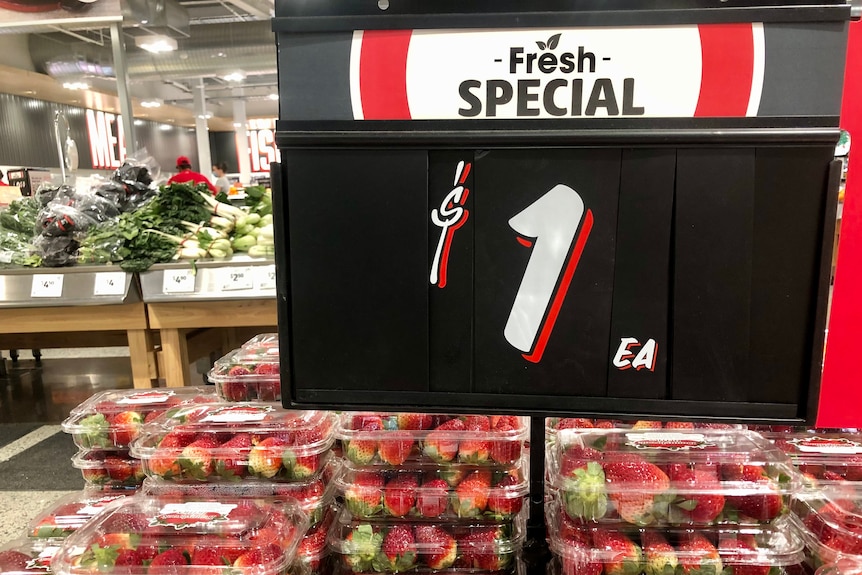 A one dollar sign above strawberries in punnets in a supermarket