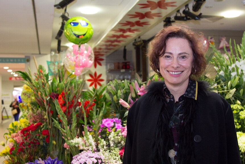 A woman stands in front of a hospital florist.