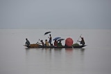 A handful of people are on a narrow kayak-style longboat as they float through waters that stretch out to the horizon.