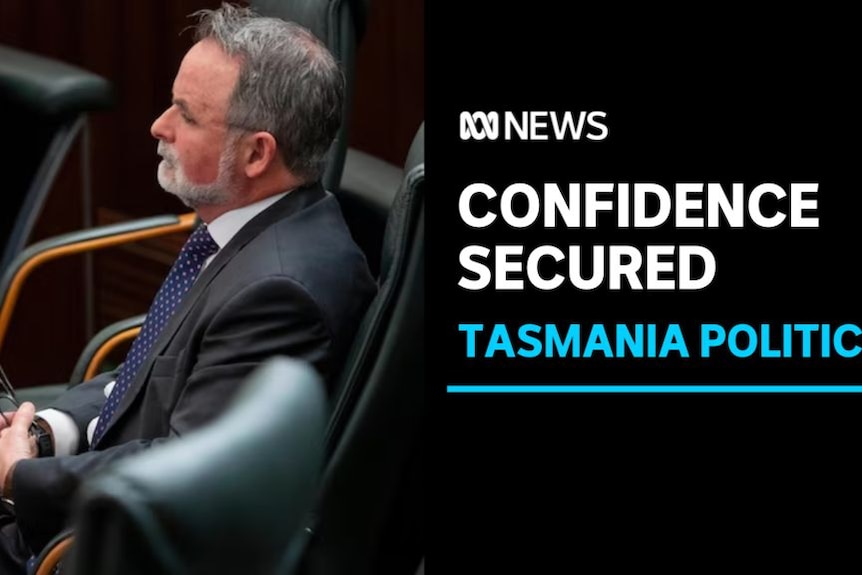 Confidence Secured, Tasmania Politics: A man in a suit sits in a chair holding glasses.