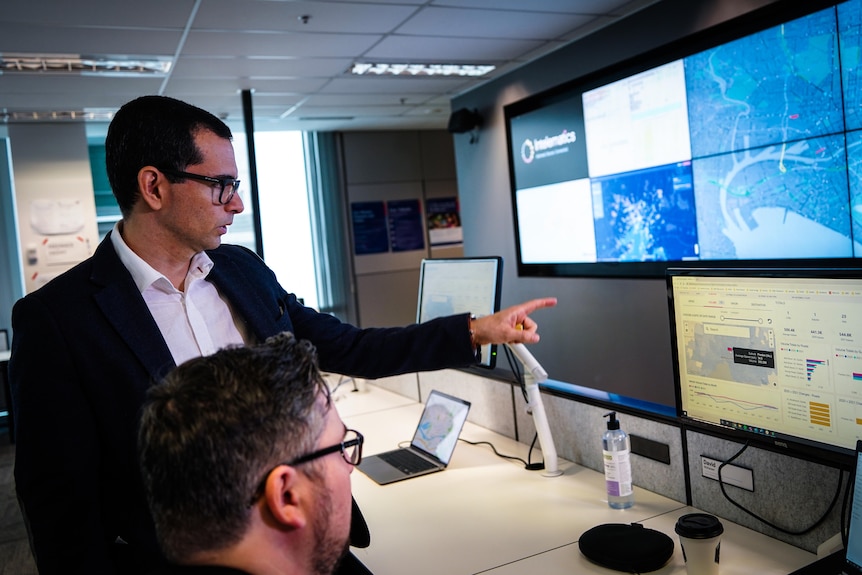 A man wearing a suit jacket points at a screen filled with traffic data