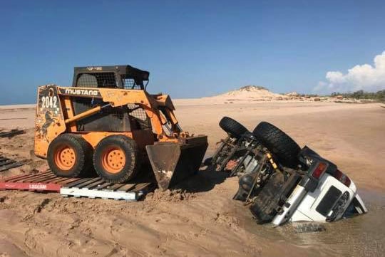 A mini mechanical digger next to an overturned four wheel drive submerged in water.