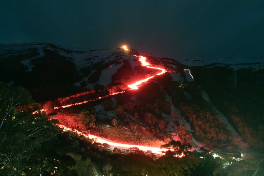 A mountain with a trail of red as skiers conduct a flare run.