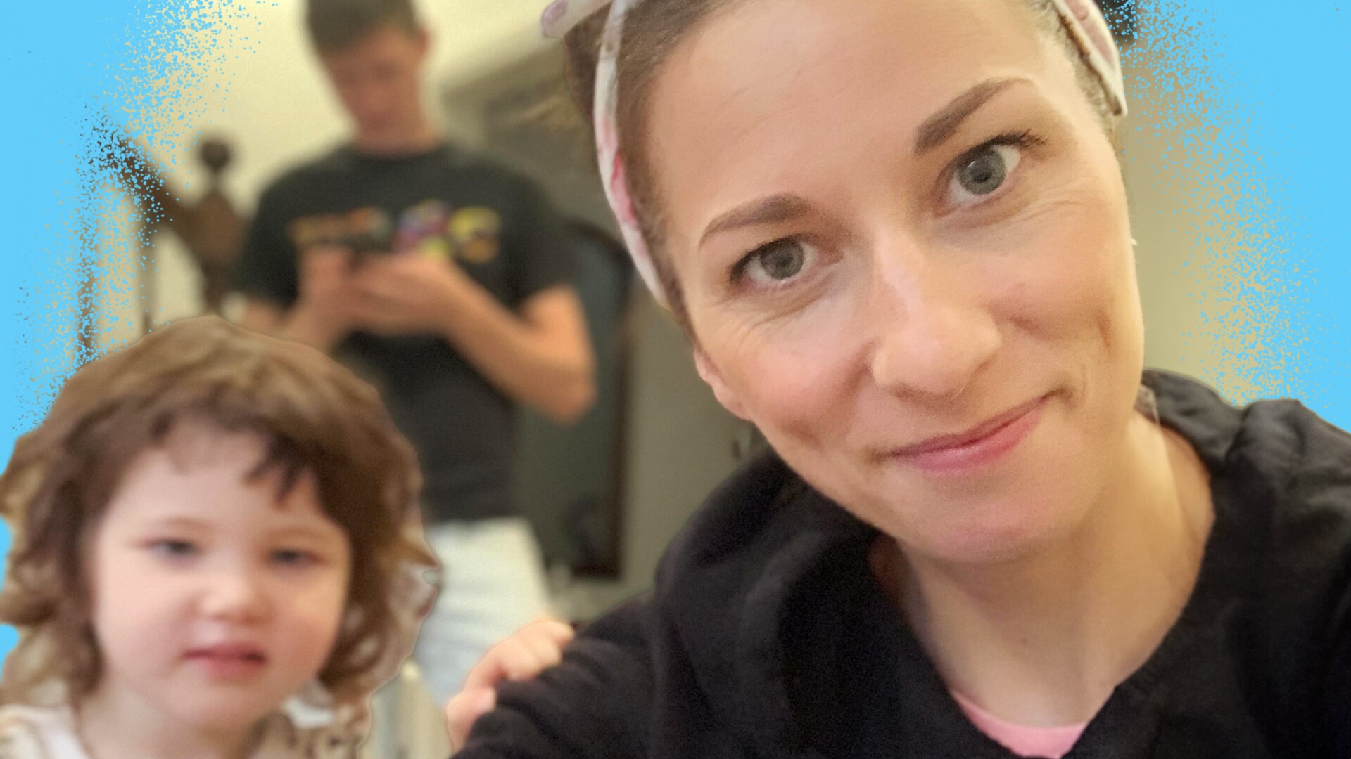 Veronica smiles at the camera as her young child and husband stand in the foreground