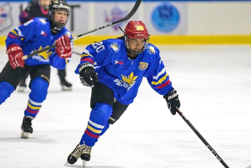 A female ice hockey player wearing full uniform and helmet is skating during a game with stick in hand.