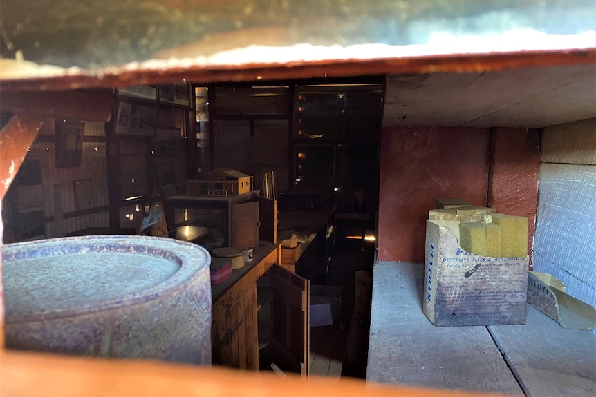 Looking inside at an old shop through the hole of an 1800s building, Christmas cake tins and other stock remain on shelves.