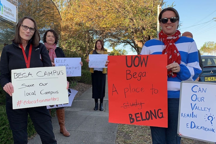 Four academic holding signs calling on the University of Wollongong to protect staff at the Bega campus.