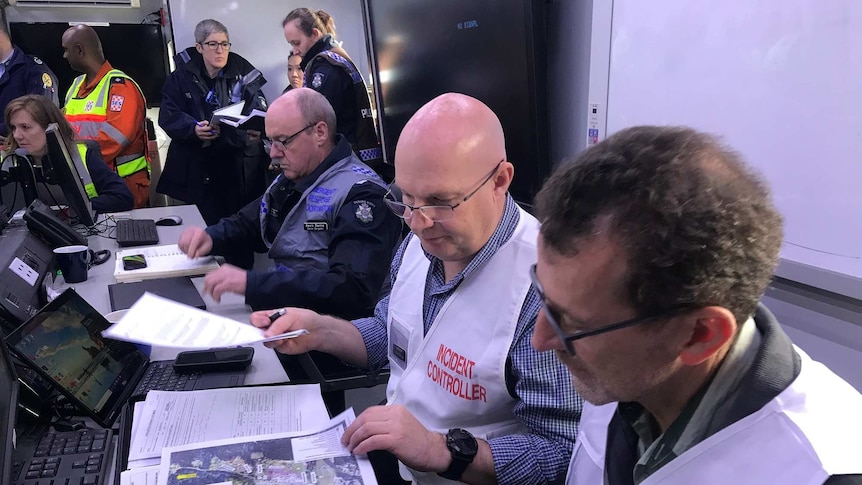 A group of people in emergency uniforms talks and looks at maps as they simulate an evacuation.