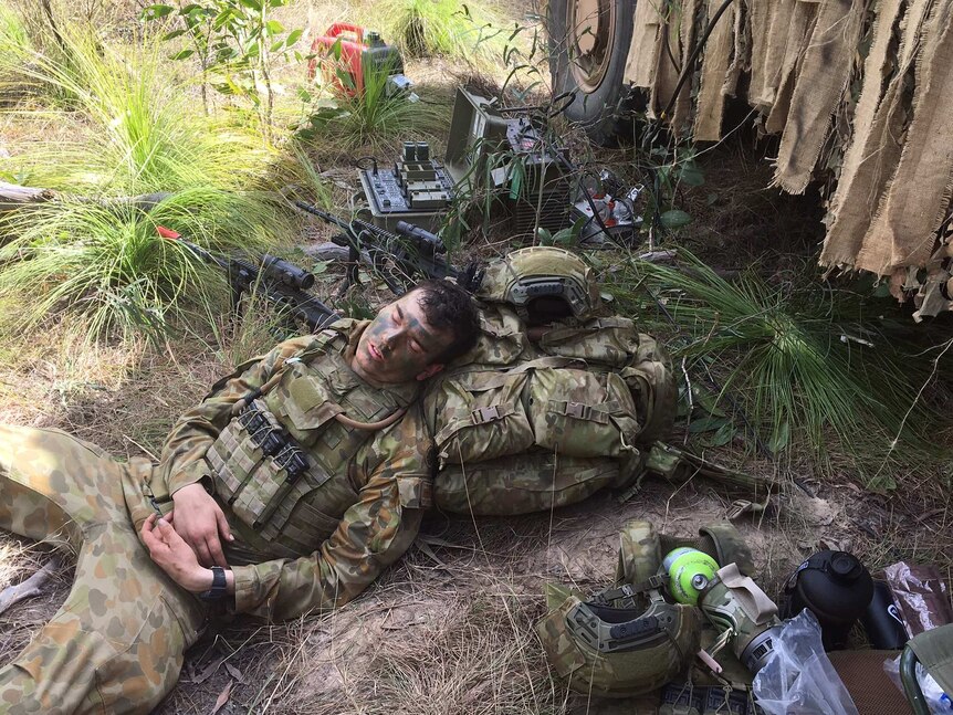 A soldier sleeps with his head resting on his backpack on the ground