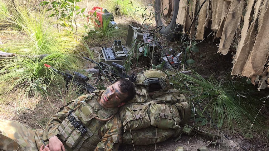 A soldier sleeps with his head resting on his backpack on the ground