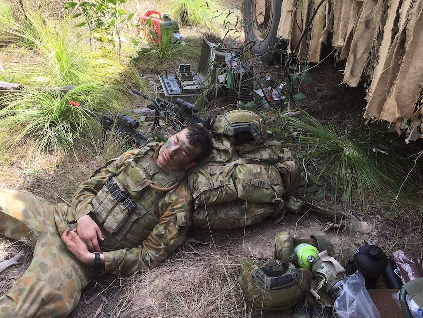 A soldier sleeps with his head resting on his backpack on the ground