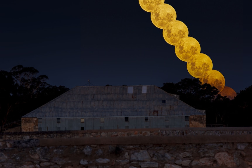 A line of yellow moons appear over a stone building under a blue night sky.