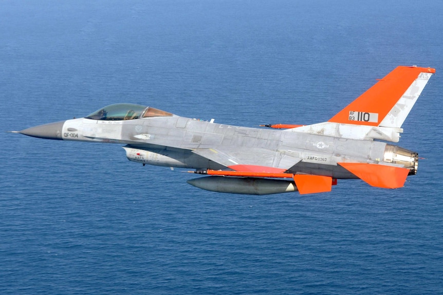An unmanned QF-16 jet flies over the ocean.
