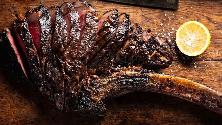 a cooked steak cut up on a board with a knife.