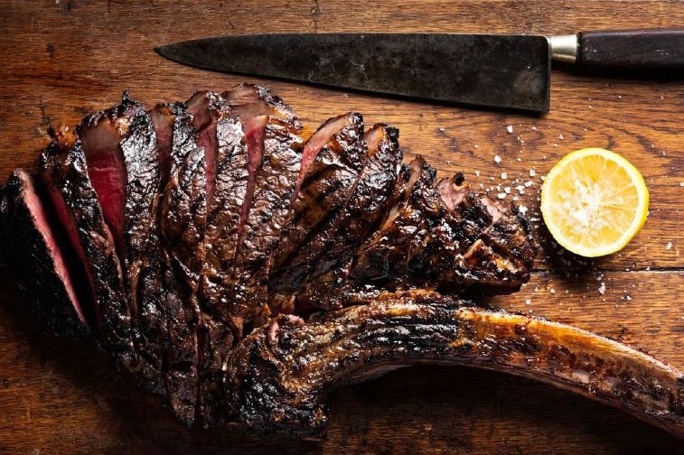 a cooked steak cut up on a board with a knife.