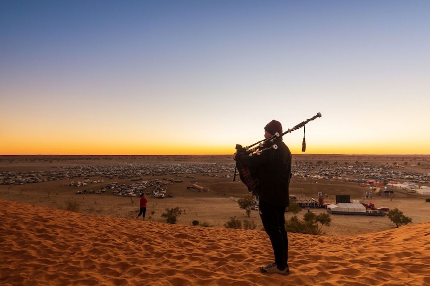 A bagpipe player stands silhouetted at sunset in the desert.