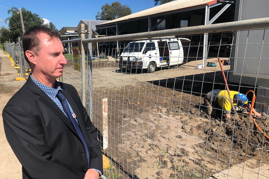 A man in a suit stands in front of a construction site.