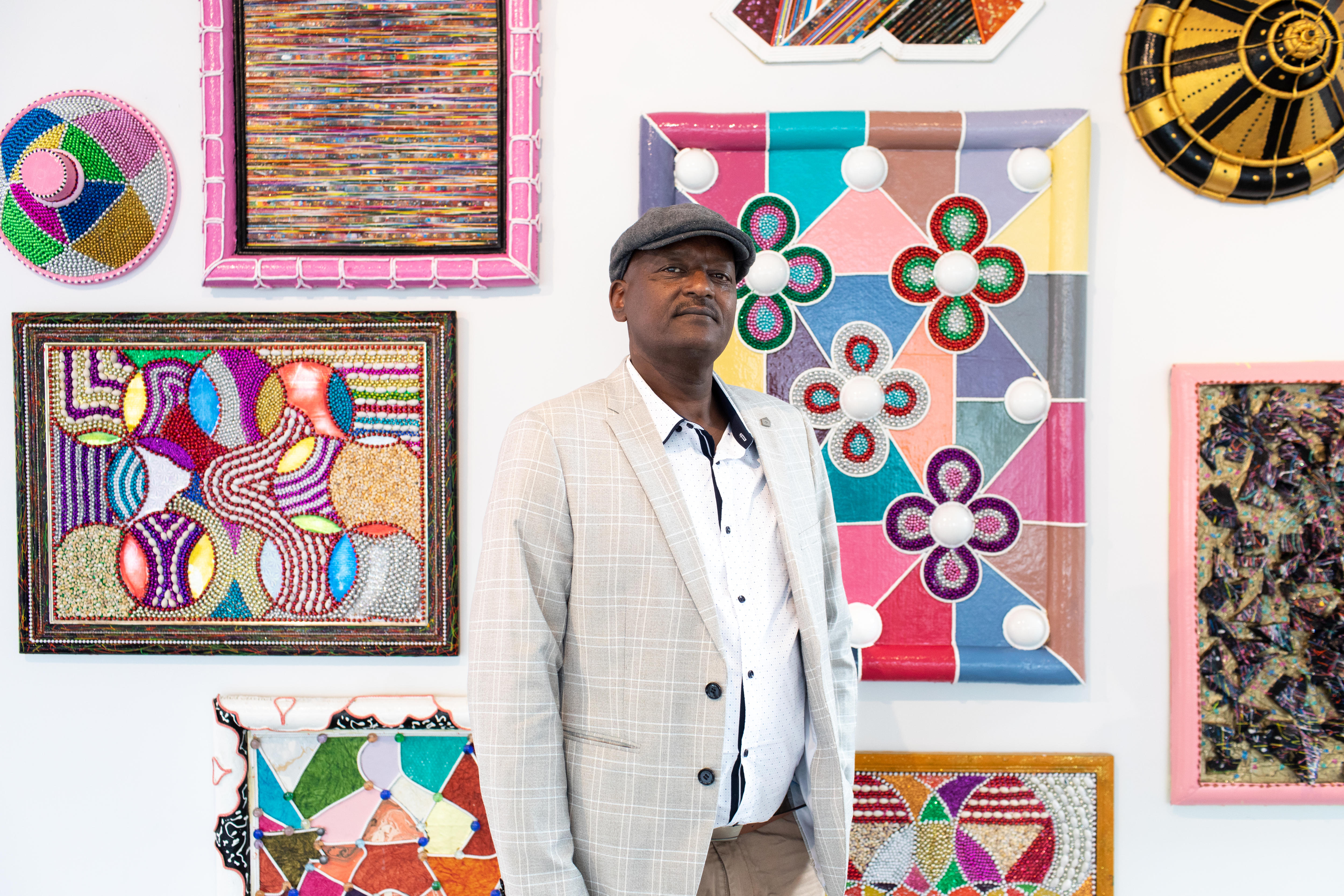 A man in a suit stands in front of brightly coloured artworks.