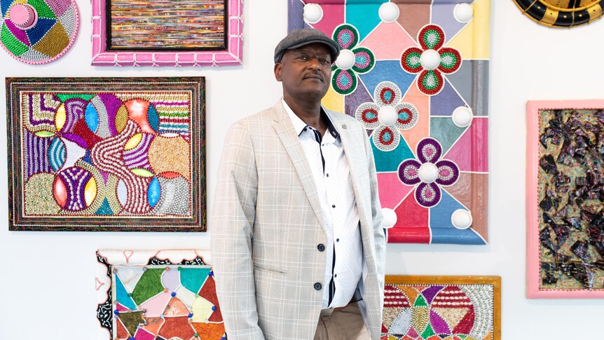 A man in a suit stands in front of brightly coloured artworks.