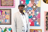 A man in a suit stands in front of brightly coloured artworks.