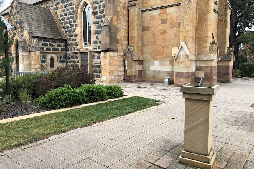 A sundial in front of a sandstone church.