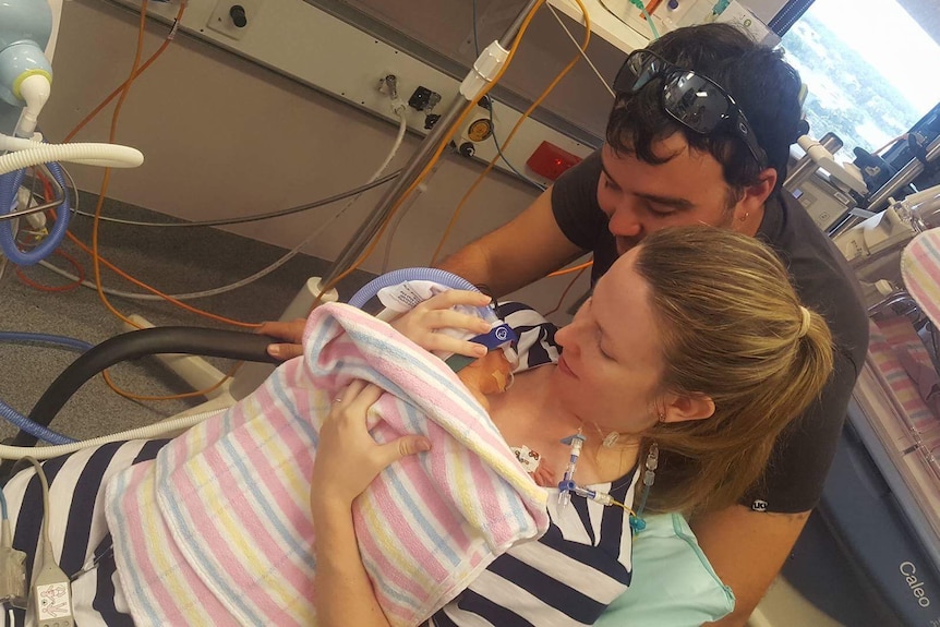 Emma and Luke Sharp hold their one week old son Caelan. He has multiple tubes and is very small.