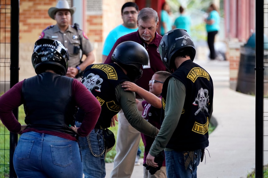 A student is hugged as he arrives at Uvalde Elementary, now protected by a fence and Texas State Troopers. 