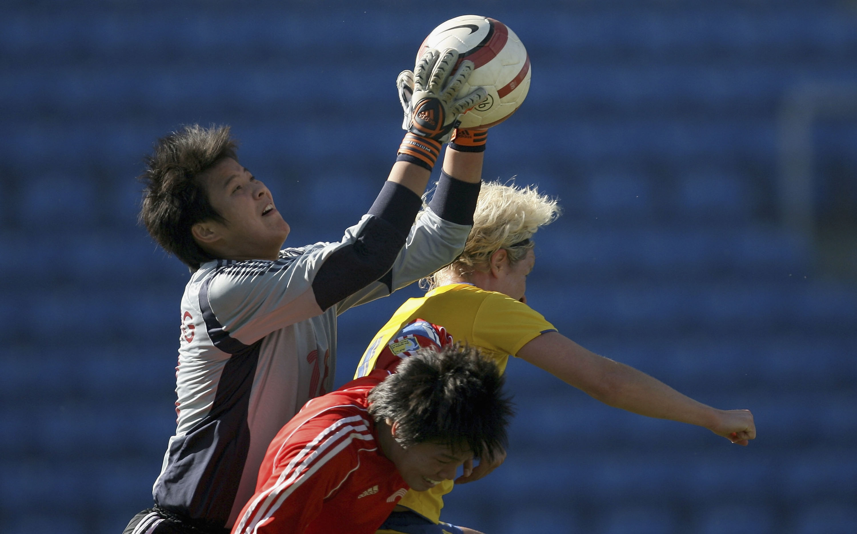Chinese goalkeeper Yanru Zhang jumps and grabs the ball over two outfield players.