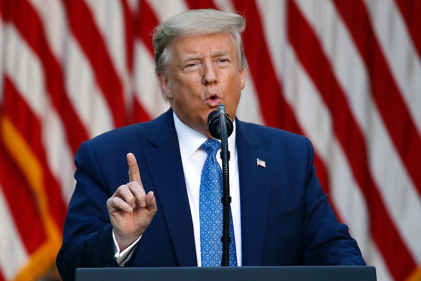 Donald Trump speaks in front of an American flag holding his finger up