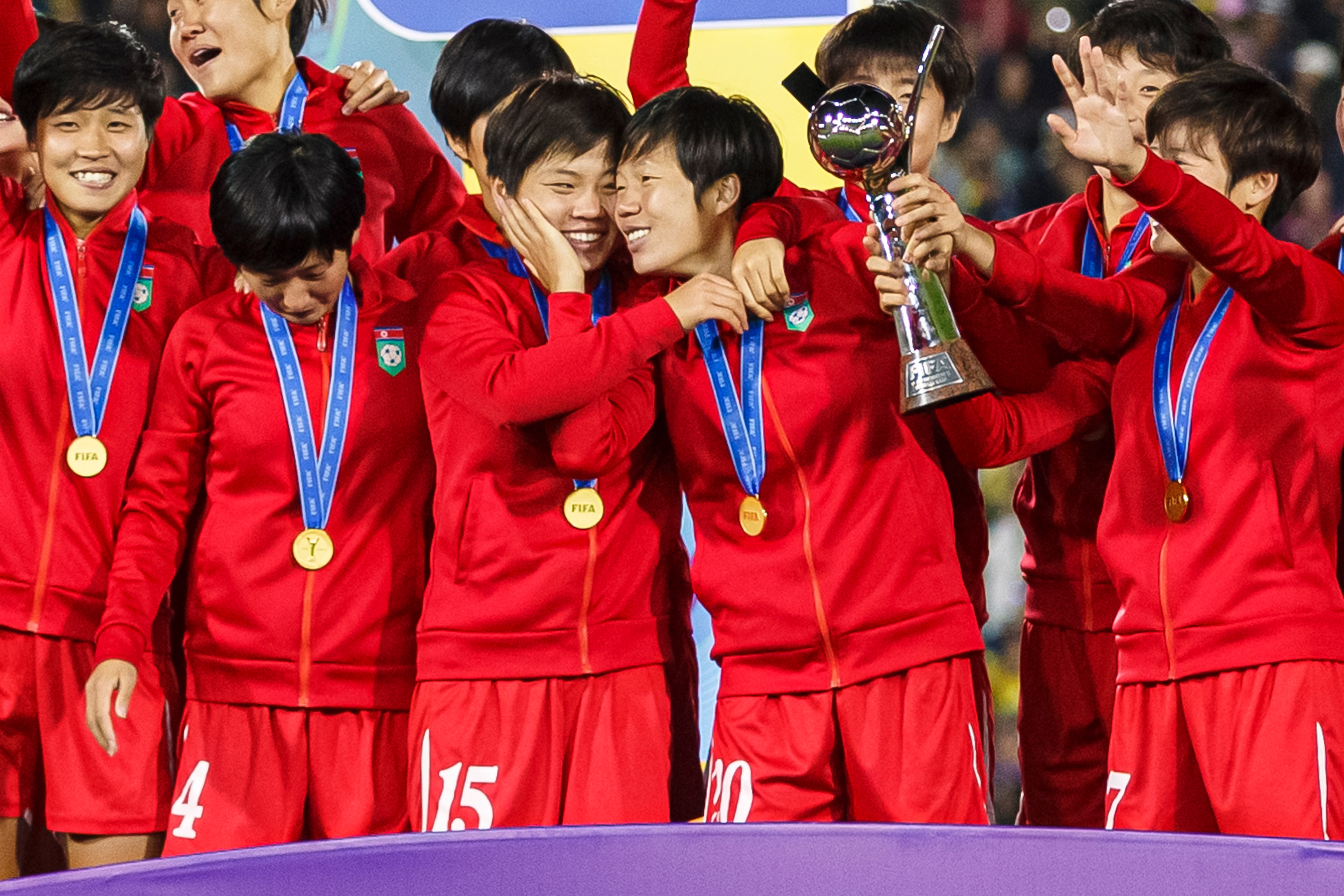 Um grupo de jogadores de vermelho comemora uma vitória no futebol e levanta um troféu