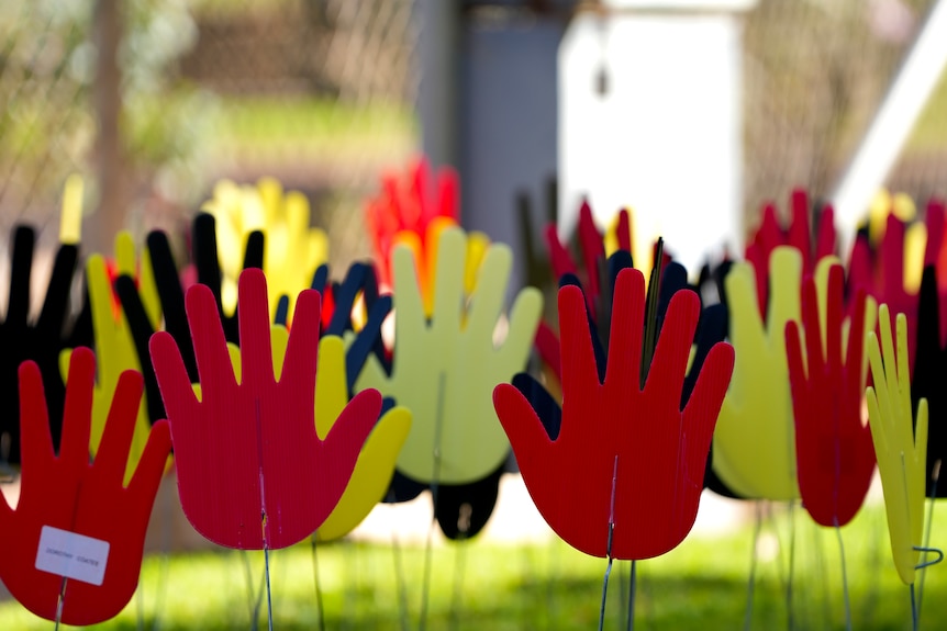 A sea of red, yellow and black hands stuck in the ground. 