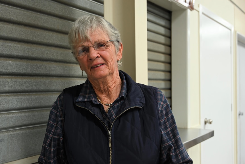 A grey-haired woman in a vest and check shirt stands in Eidsvold Community Hall after a meeting.