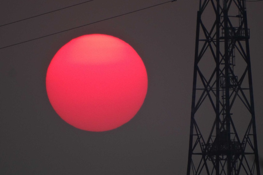 A bright red sun sets against a greyish sky and powerlines.