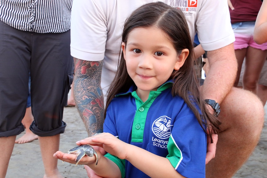 A young girl holds a baby sea turtle at Casuarina Beach in Darwin