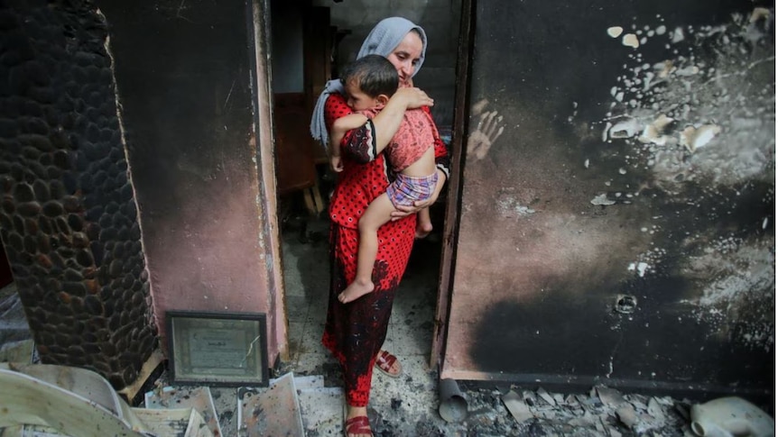 a woman holding a small child in the doorway of a burnt out home