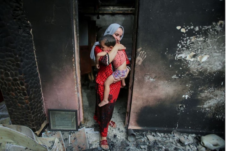 a woman holding a small child in the doorway of a burnt out home