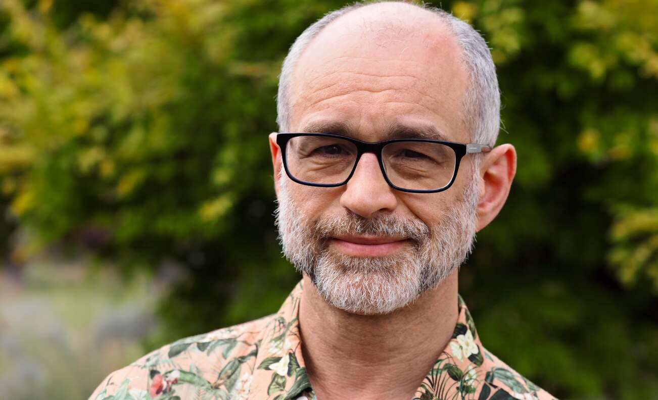 Portrait of Michael Barnett. He wears glasses and wears a floral shirt.