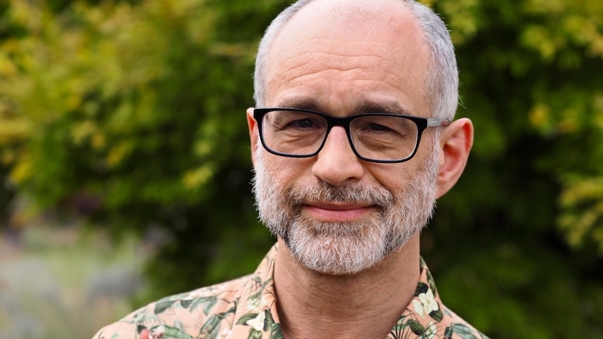 Portrait of Michael Barnett. He wears glasses and wears a floral shirt.