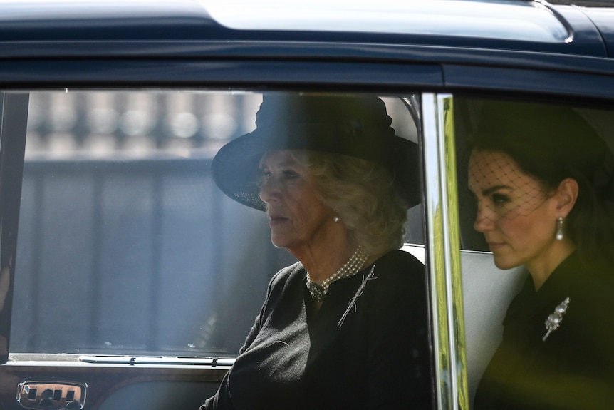 Queen Consort Camilla and Princess Kate in the back of a car dressed in black. 
